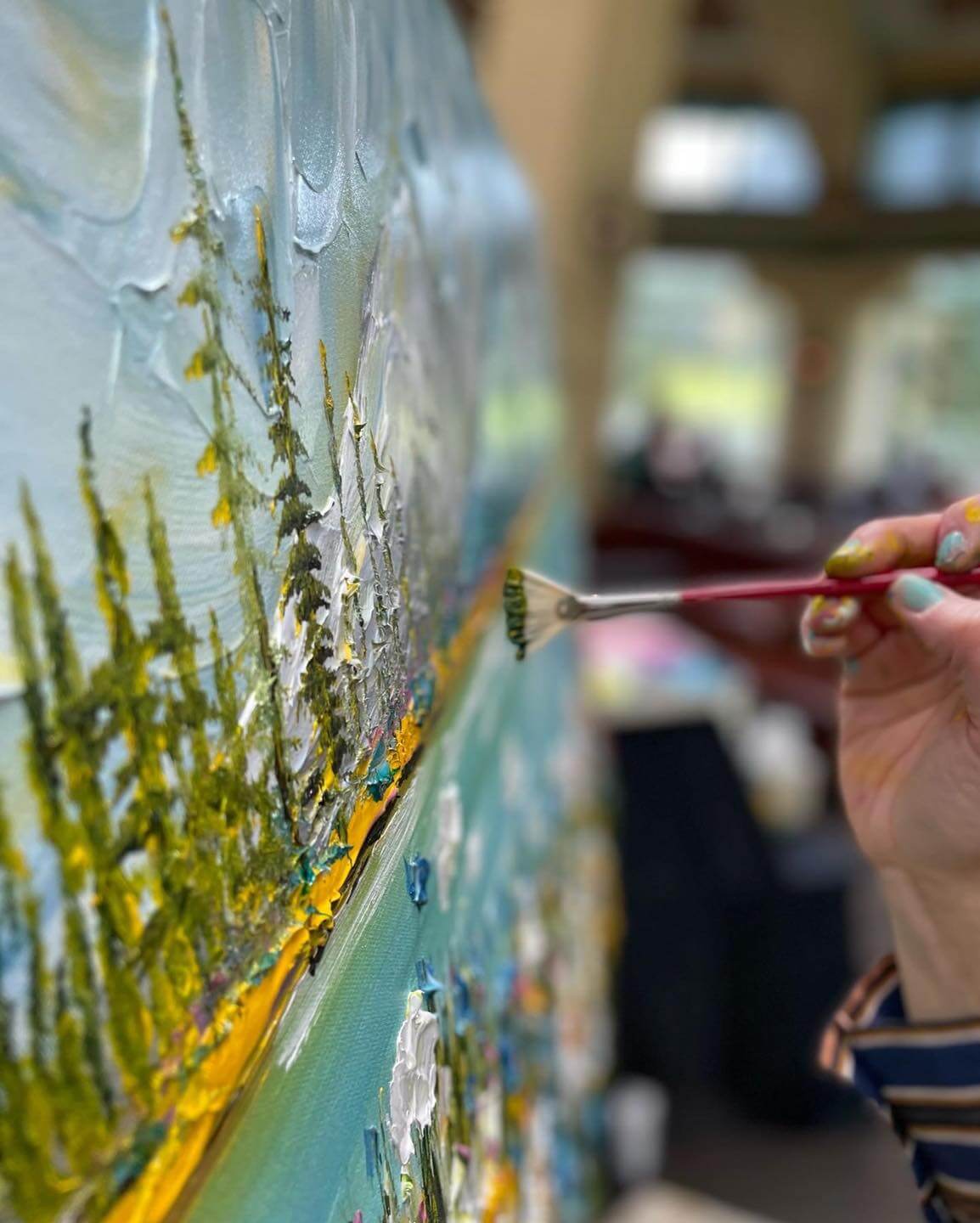 Photograph of Giselle's creative processe. The focus of the image is on her hand as she uses her little brush to add some soft touches on the painting she is working on.