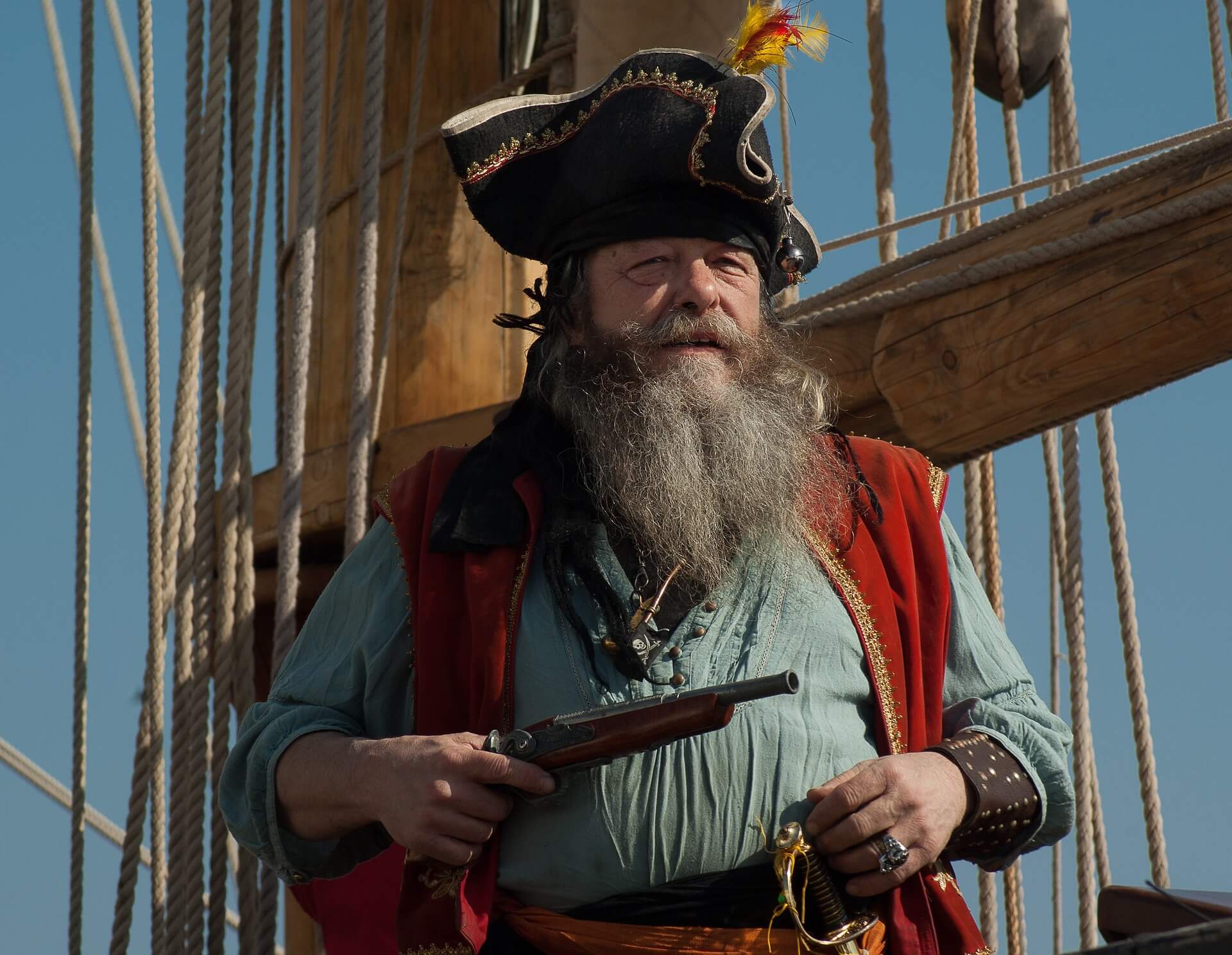 Photograph of an old man dressed as a pirate on a ship, holding in his hand a pistol.
