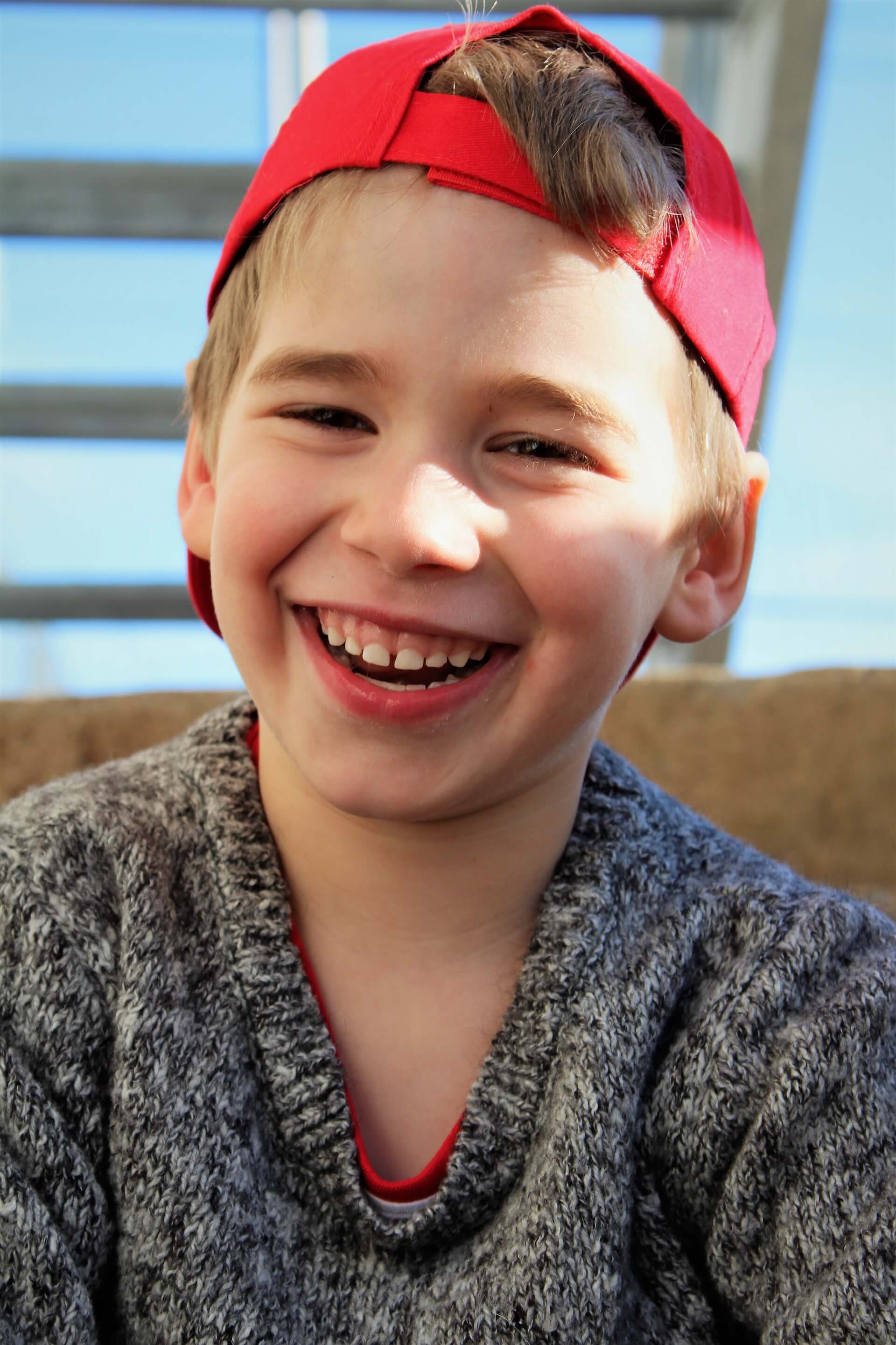 Photograph of a young boy wearing a hat and laughing at the camera.